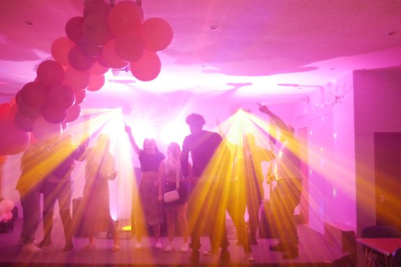 with Silhouettes of people dancing under bright pink and yellow stage lights at a party.